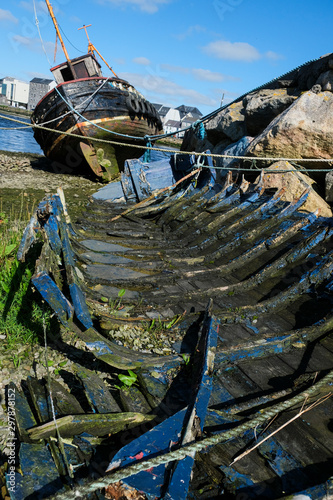 Old wooden shipwreck at the edge of the Corrib River as it flows into Galway Bay, Ireland showing the decayed wood, and houses in the background, taken on a sunny summer day.