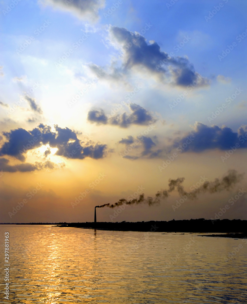 Sunset on the Rupsa River (Rupsha River) near Khulna, Bangladesh. Taken on the river between Khulna and the Sundarban Forest. The contrast of nature and the smokestack illustrates environmental damage