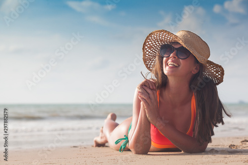 Beach woman funky happy and colorful wearing sunglasses and beach hat having summer fun during travel holidays vacation. Young trendy cool hipster woman in bikini lying in the sand.