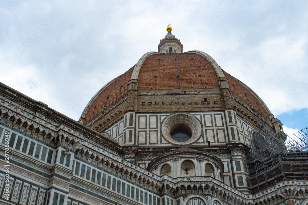 Florence's Santa Maria del Fiore Dome close seen from the side with clouds and blue sky.