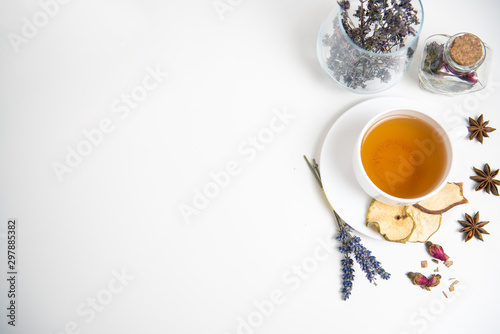 a white mug on a white table with herbal tea and herbal ingredients laid out on the table. Concept on the topic of herbal treatment for colds and flu in autumn. Top view