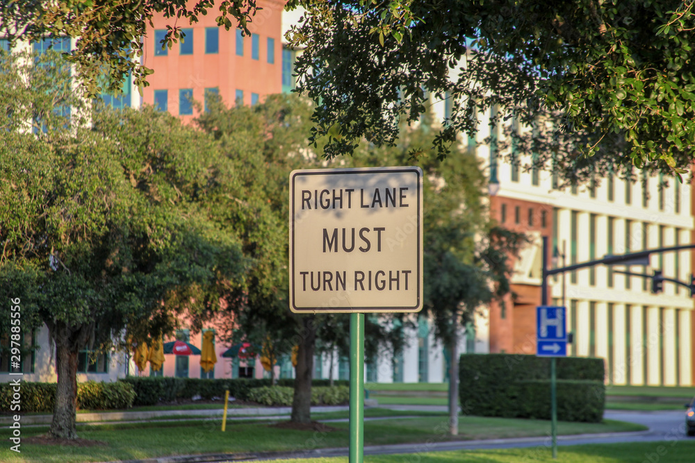 A sign stating that: right lane should turn right. In the background, a huge beautiful building, trees and shrubs in the late afternoon in Celebration, Florida