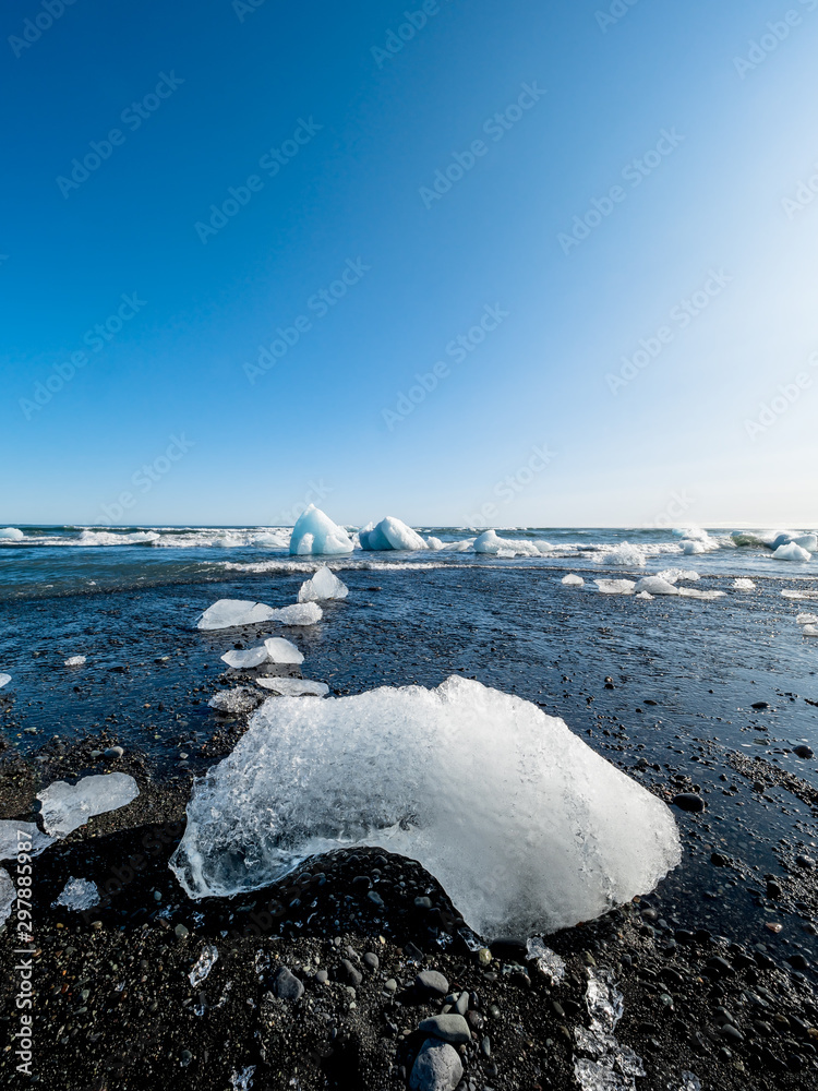 Big ice on black sand, part of an iceberg from Jokulsarlon glacier in  Diamond beach, one of the most touristic spots in Iceland. Photos | Adobe  Stock