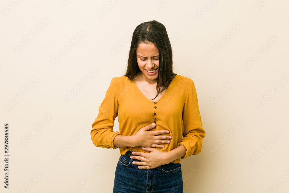 Young hispanic woman against a beige background sick, suffering from stomachache, painful disease concept. Young hispanic woman against a beige background sick, suffering from stomachache, painful disease concept.