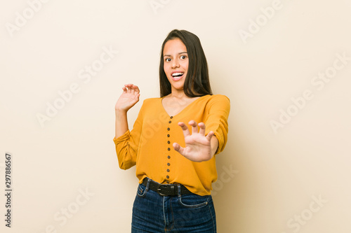 Young hispanic woman against a beige background being shocked due to an imminent danger