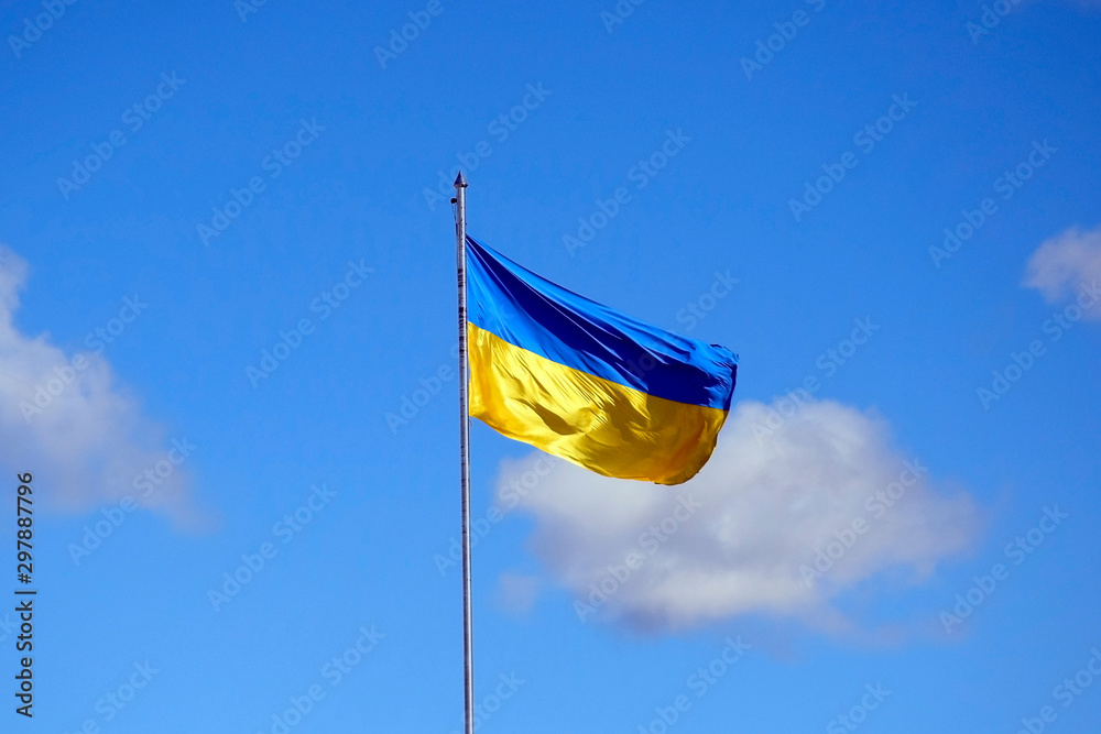 Ukrainian flag on flagpole against the blue cloudless sky. The official flag of the Ukrainian state includes yellow and blue color. Flag waving in the wind. Selective focus.