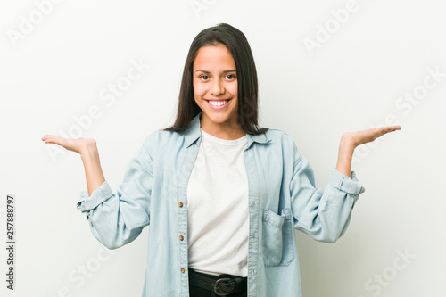 Young hispanic woman makes scale with arms, feels happy and confident.