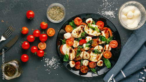 Italian caprese salad with chopped tomatoes, mozzarella cheese, basil, spices, balsamic vinegar and olive oil. Vegetarian dish. dark concrete background photo