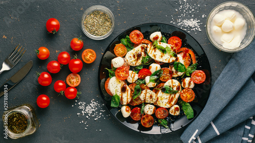 Italian caprese salad with chopped tomatoes, mozzarella cheese, basil, spices, balsamic vinegar and olive oil. Vegetarian dish. dark concrete background
