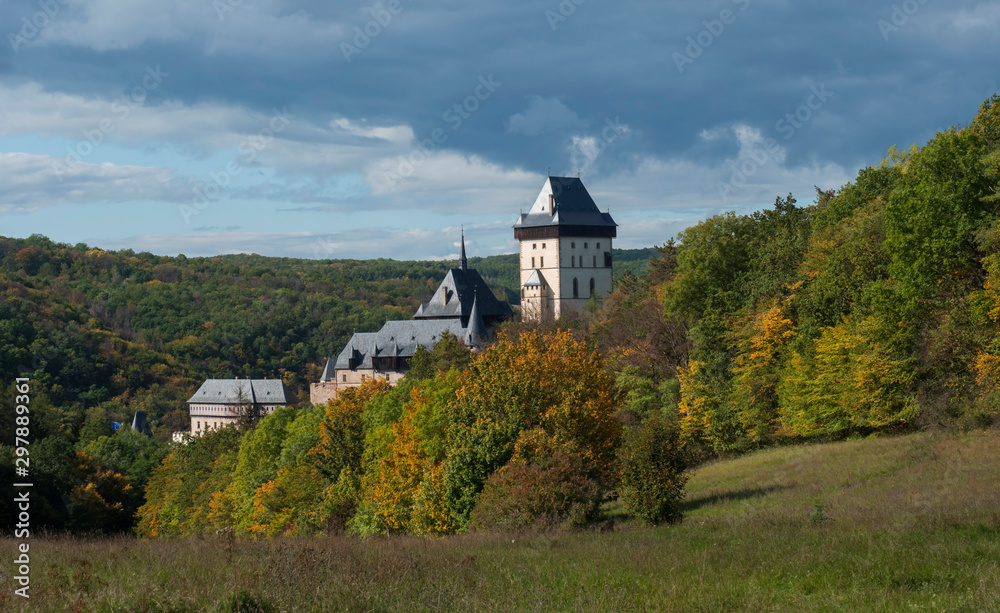 Fototapeta premium Karlstejn gothic state castle near Prague, the most famous castle in Czech Republic with grass meadow and autumn colored trees and forest. Blue sky clouds background. Located near Prague.