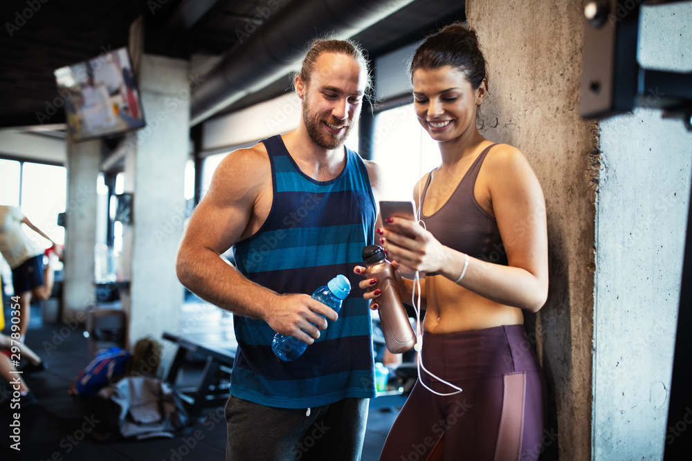 Obraz premium Young sporty woman showing something on smart phone to her male friend in a gym.