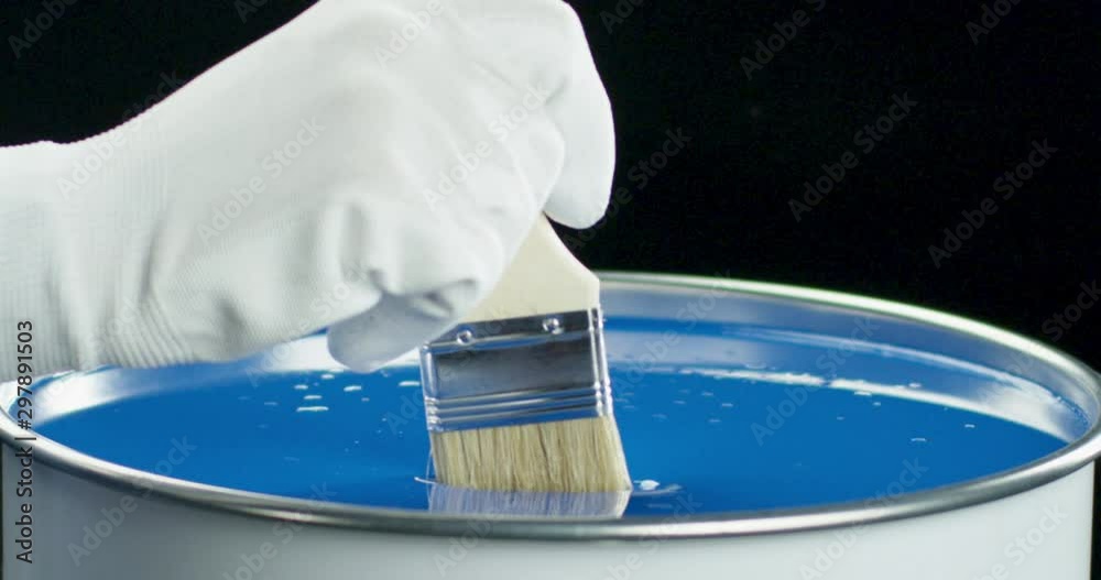 Decorator dipping brush into can with blue paint slow motion closeup.