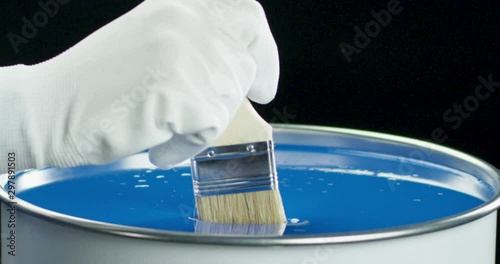 Decorator dipping brush into can with blue paint slow motion closeup.