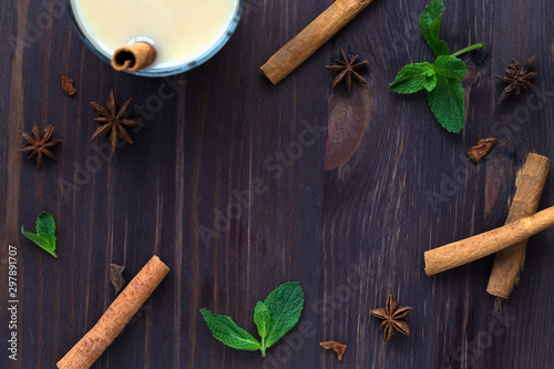 Fototapeta Naklejka Na Ścianę i Meble -  Cup of tea with milk with spices on wooden dark background. spices: anise stars and cinnamon with mint. christmas decoration. Healthy lifestyle. masala tea. top view with copy space in the centr