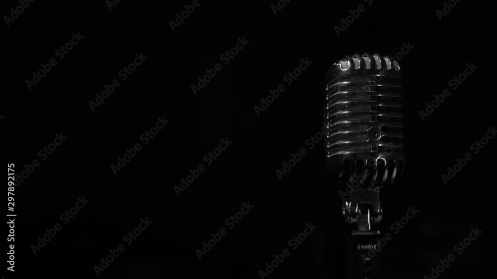 Glare of white light flickers and shine on a chrome retro mic on right on black background. Professional vintage glare microphone for record or speak to audience on stage in dark empty club close up.