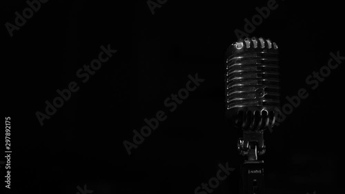Glare of white light flickers and shine on a chrome retro mic on right on black background. Professional vintage glare microphone for record or speak to audience on stage in dark empty club close up.