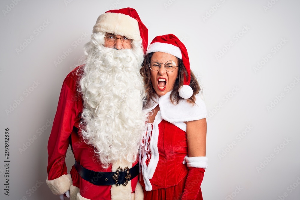 Middle age couple wearing Santa costume hugging over isolated white background angry and mad screaming frustrated and furious, shouting with anger. Rage and aggressive concept. Middle age couple wearing Santa costume hugging over isolated white background angry and mad screaming frustrated and furious, shouting with anger. Rage and aggressive concept.