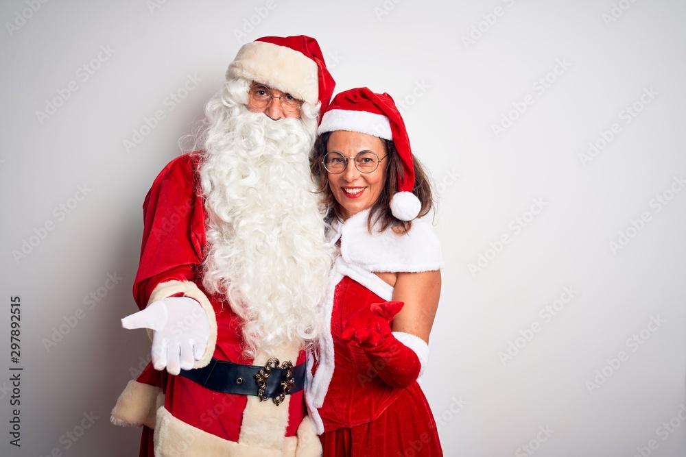 Middle age couple wearing Santa costume hugging over isolated white background smiling cheerful offering palm hand giving assistance and acceptance. Middle age couple wearing Santa costume hugging over isolated white background smiling cheerful offering palm hand giving assistance and acceptance.