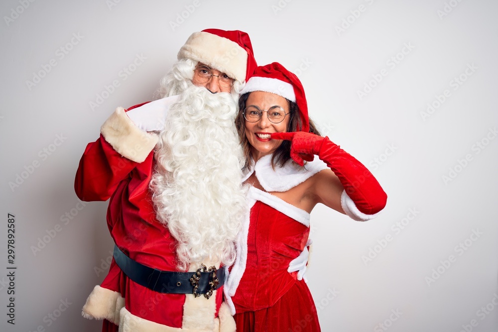 Middle age couple wearing Santa costume hugging over isolated white background smiling cheerful showing and pointing with fingers teeth and mouth. Dental health concept. Middle age couple wearing Santa costume hugging over isolated white background smiling cheerful showing and pointing with fingers teeth and mouth. Dental health concept.