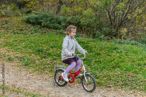 Little happy girl child rides a bicycle in the autumn forest