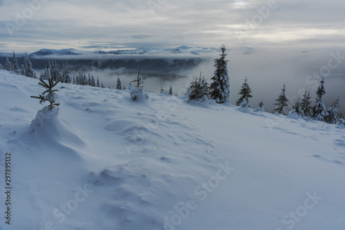 Magic winter fogs in Ukrainian Carpathians overlooking the snow-capped mountain peaks from the picturesque mountain valley with tourists in tents. © reme80