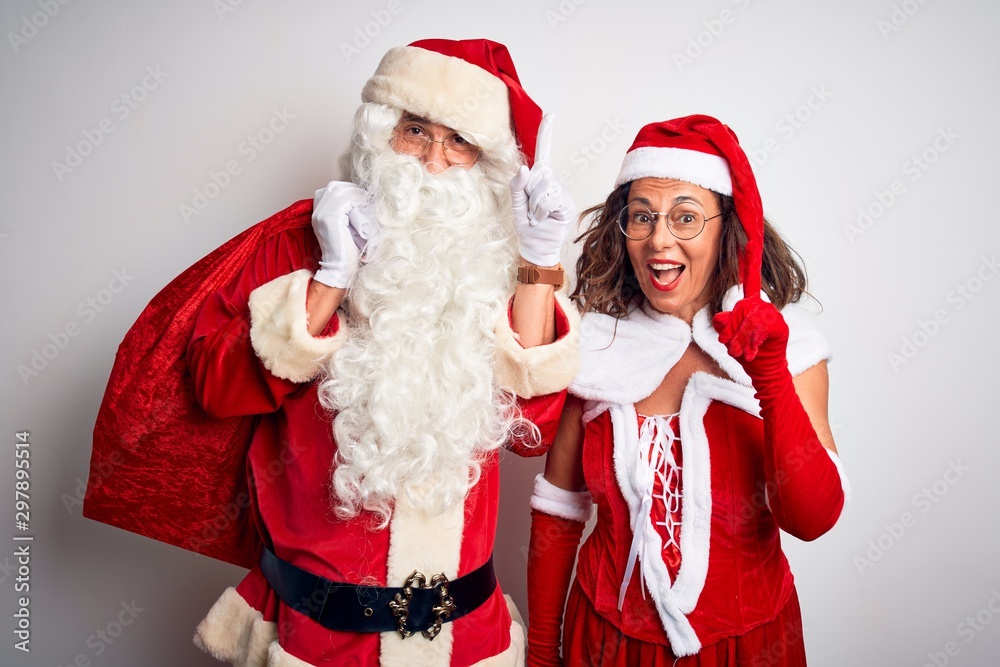 Senior couple wearing Santa Claus costume holding sack over isolated white background surprised with an idea or question pointing finger with happy face, number one Senior couple wearing Santa Claus costume holding sack over isolated white background surprised with an idea or question pointing finger with happy face, number one