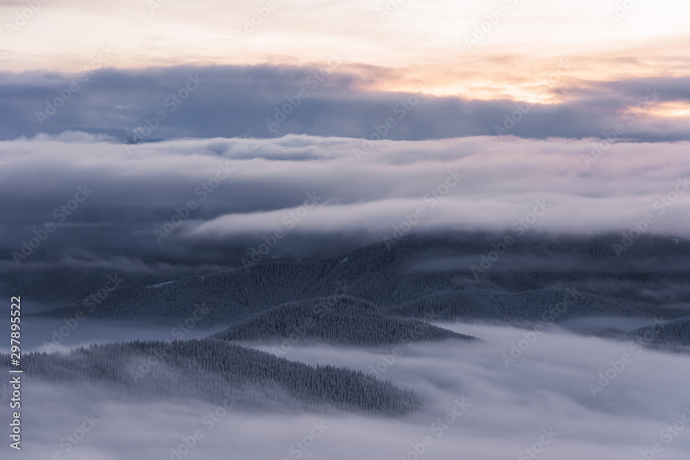 Magic winter fogs in Ukrainian Carpathians overlooking the snow-capped mountain peaks from the picturesque mountain valley with tourists in tents.