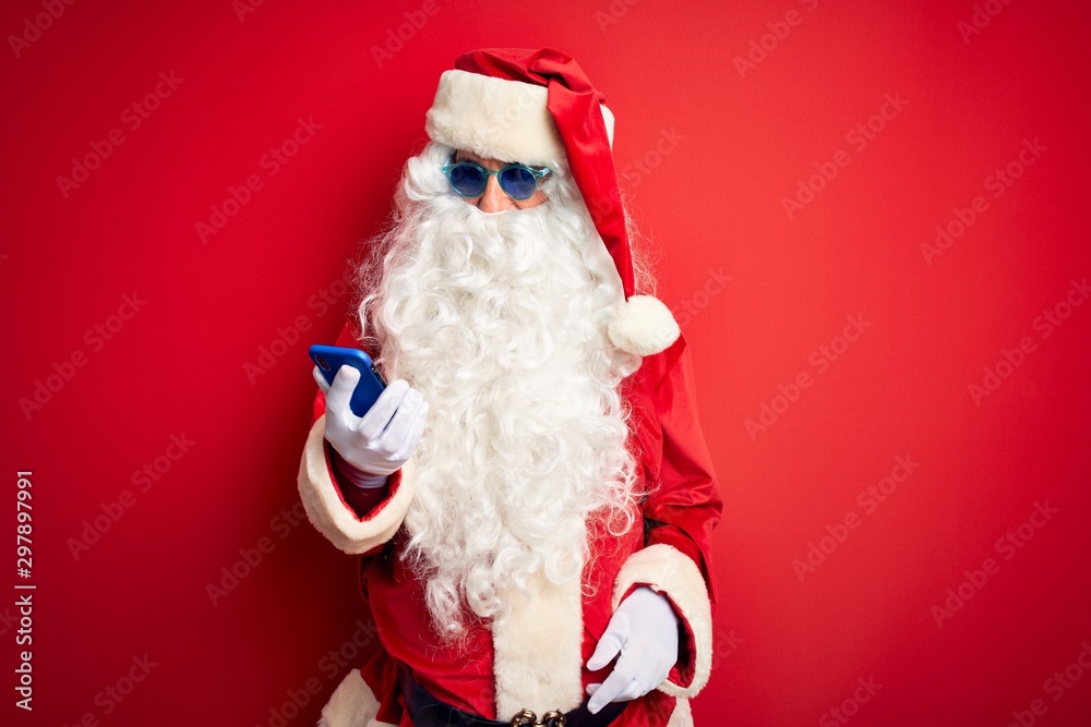 Senior man wearing Santa Claus costume using smartphone over isolated red background with a confident expression on smart face thinking serious
