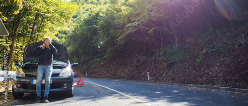 A broken car on the road, the driver holds an open hood and watches what has broken down, a roadside assistance is waiting