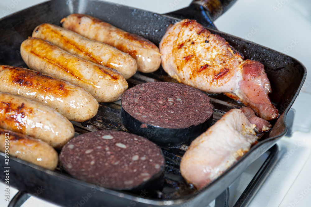 Sausages, bacon and black pudding cooking in a griddle pan Stock Photo