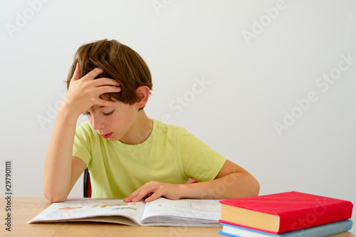 Boy does his homework at his desk at home. The student / pupil has been bored on the lesson. First grader.