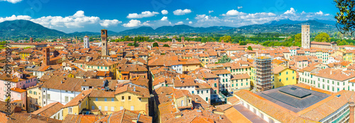 Aerial top panoramic view of historical centre medieval town Lucca with old buildings, typical orange terracotta tiled roofs and mountain range, hills, blue sky white clouds background, Tuscany, Italy