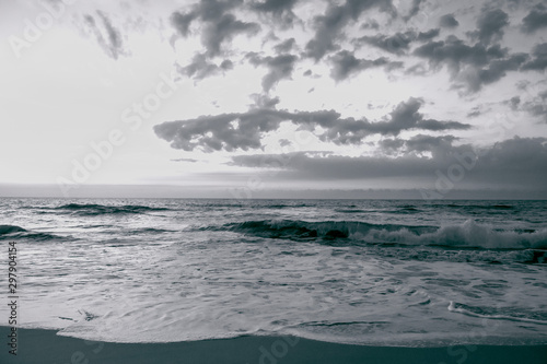 Dramatic clouds hang over the ocean at sunrise in this black and white photo