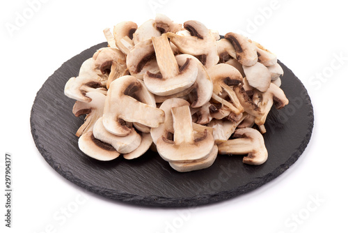 Fresh sliced champignon mushrooms on a stone plate, isolated on white background