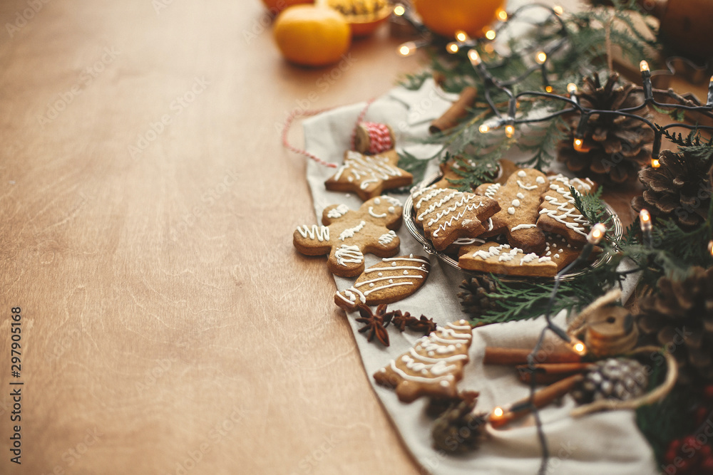 Fototapeta premium Merry Christmas. Festive gingerbread cookies with anise, cinnamon, pine cones, cedar branches and golden lights bokeh on rustic table. Space for text. Atmospheric image.