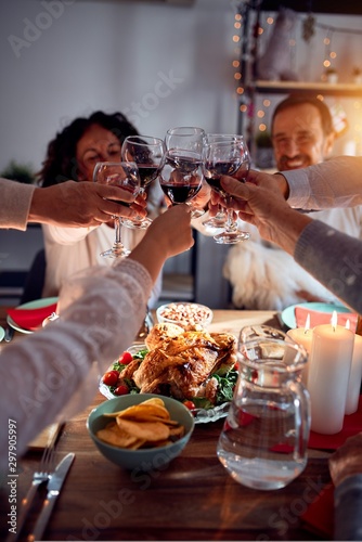 Family and friends dining at home celebrating christmas eve with traditional food and decoration, making a toast with best wishes with glass of wine