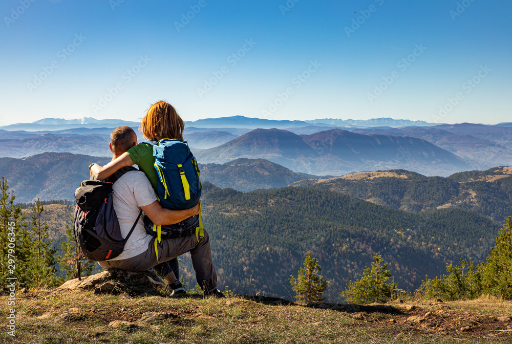 Rear view of hikers couple with backpack sitting on top of the mountain and enjoying the view during the day.