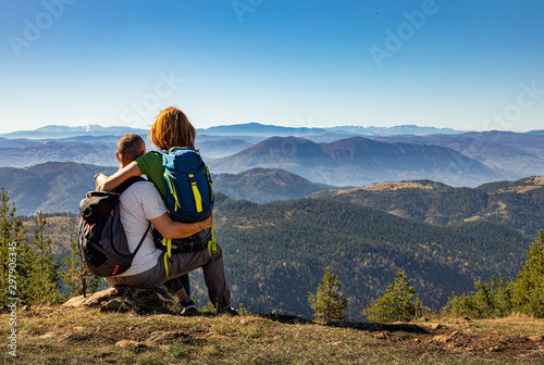 Rear view of hikers couple with backpack sitting on top of the mountain and enjoying the view during the day.