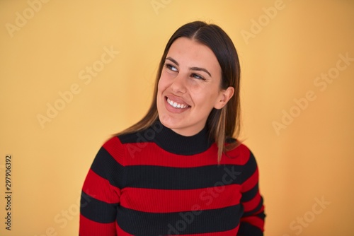 Young beautiful woman smiling happy wearing a sweater over isolated yellow background © Krakenimages.com