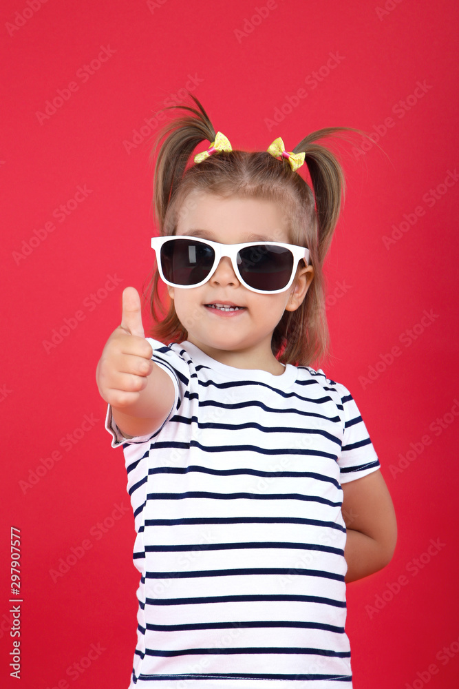 Cute little girl in sunglasses showing thumb up on red background Cute little girl in sunglasses showing thumb up on red background