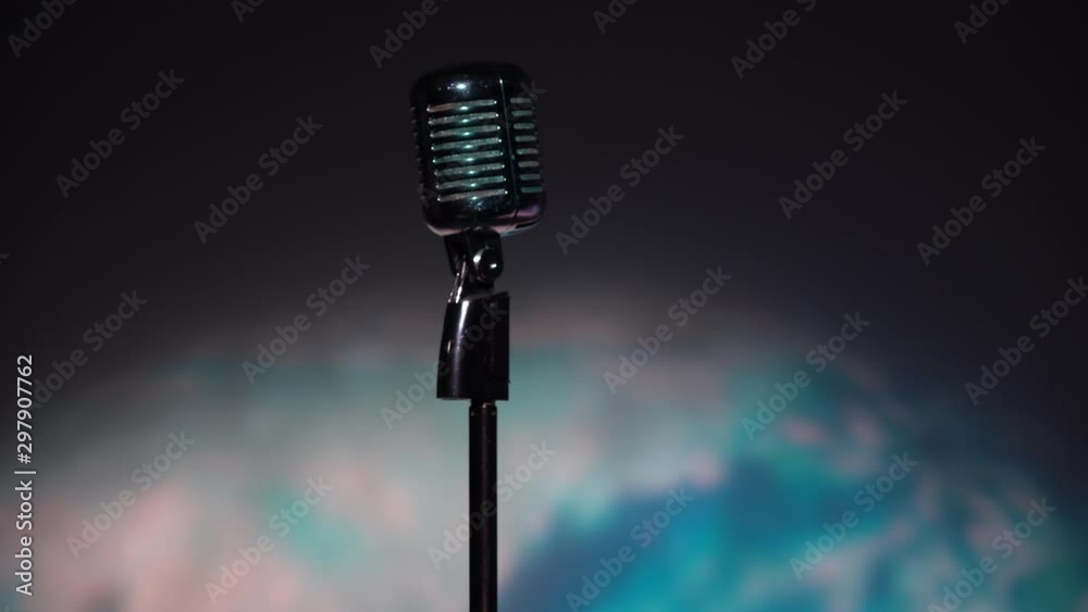 Young Caucasian man in a white open shirt with short hair lowers, regulate and fix the classic retro glare microphone on scene in dark club close up. Male walks away from stage. Spotlights shine.