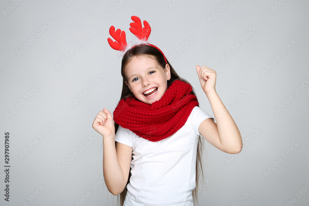 Little girl in christmas red horns and knitted scarf on grey background Little girl in christmas red horns and knitted scarf on grey background