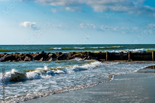 Ocean waves rush the shoreline on a bright day with blue sky and clouds