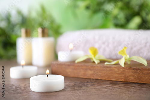 Composition with burning candles and flowers on wooden table against blurred background, space for text. Spa concept
