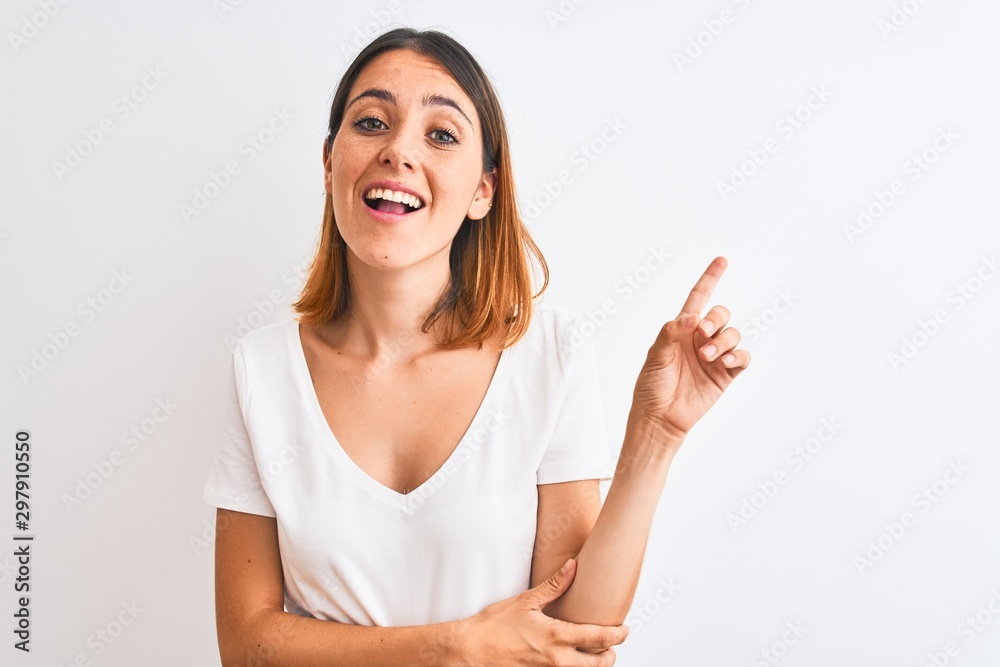 Beautiful redhead woman wearing casual white t-shirt over isolated background with a big smile on face, pointing with hand and finger to the side looking at the camera. Beautiful redhead woman wearing casual white t-shirt over isolated background with a big smile on face, pointing with hand and finger to the side looking at the camera.