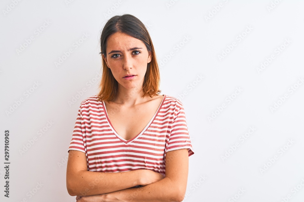 Beautiful redhead woman wearing casual striped red t-shirt over isolated background skeptic and nervous, disapproving expression on face with crossed arms. Negative person. Beautiful redhead woman wearing casual striped red t-shirt over isolated background skeptic and nervous, disapproving expression on face with crossed arms. Negative person.