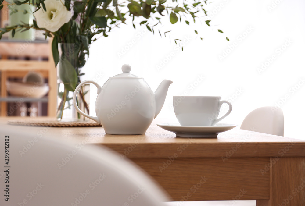 Obraz premium Teapot, cup and flowers on wooden dining table indoors. Kitchen interior