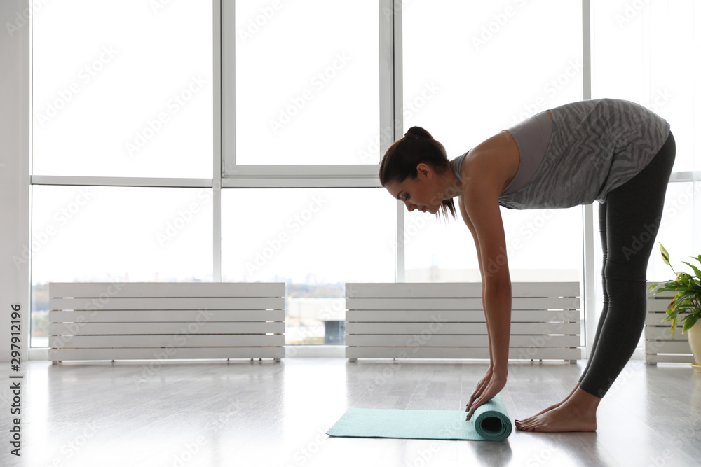 Young woman unrolling mat in yoga studio Young woman unrolling mat in yoga studio