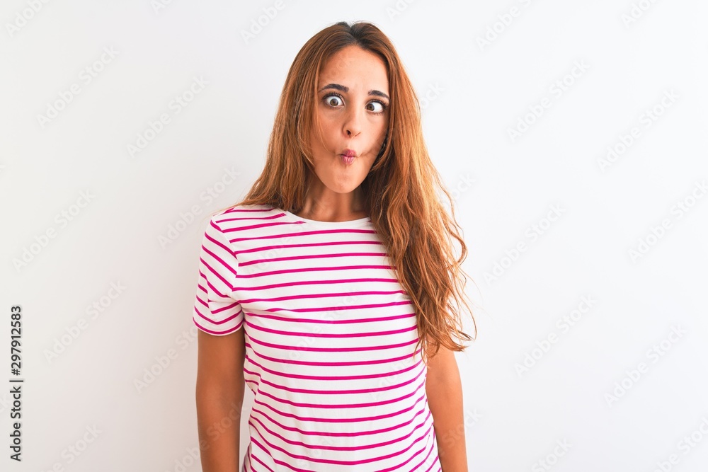 Young redhead woman wearing striped casual t-shirt stading over white isolated background making fish face with lips, crazy and comical gesture. Funny expression. Young redhead woman wearing striped casual t-shirt stading over white isolated background making fish face with lips, crazy and comical gesture. Funny expression.