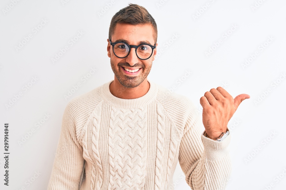 Naklejka premium Young handsome man wearing glasses and winter sweater over isolated background pointing and showing with thumb up to the side with happy face smiling